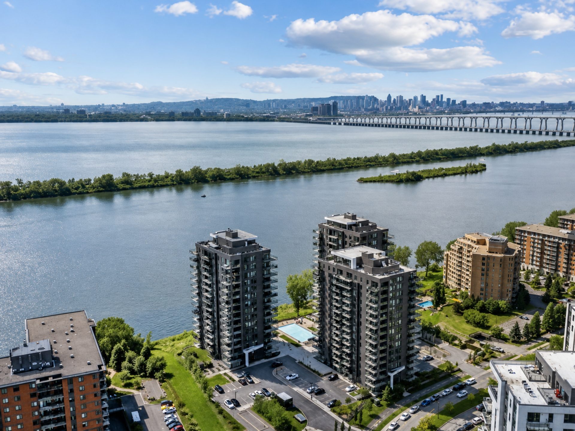 Vue aérienne des tours du LUM Pur Fleuve au bord du fleuve Saint-Laurent, avec la silhouette de Montréal à l'horizon